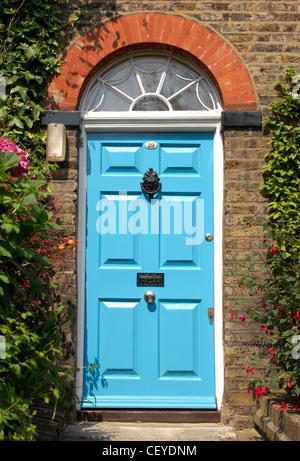 Blue painted front dowith black knocker, letterbox and knob, semi circle arch window above dowith red brick arch and ivy Stock Photo