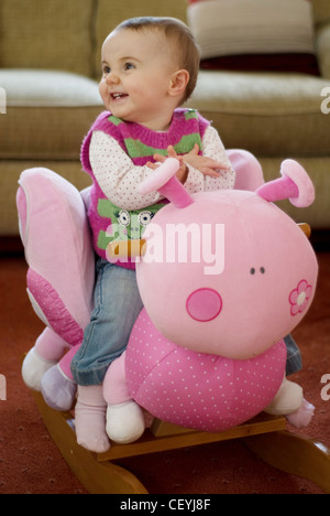 A female baby fair hair, wearing a white polka dot top, pink and green striped vest, jeans and pink socks, sitting on a Stock Photo