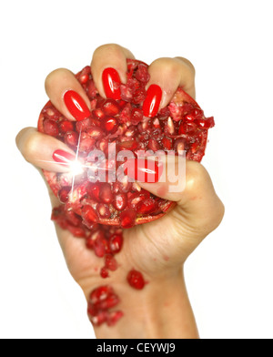 Female wearing bright red nail varnish squashing a pomegranate in the palm of her hand Stock Photo