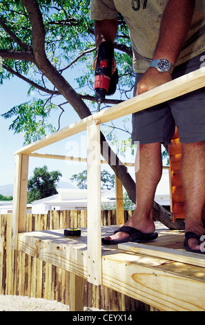 FORBuild a Tree House Step Male screwing a plank of wood to the base of the tree house to create safety railings Stock Photo