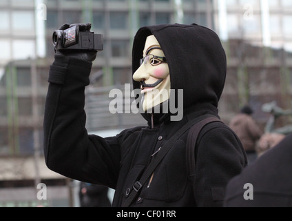 An Anonymous member with a Guy Fawkes mask is recording a protest with a small video cam. Stock Photo