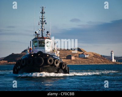 A tug boat passes the lighthouse on George's Island in Halifax, Nova Scotia, Canada. Stock Photo