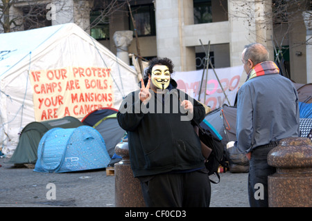 A masked member of Anonymous, part of the peaceful Occupy London protest, in front of tents outside St Paul's Cathedral. Stock Photo