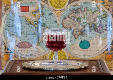 wine glass on silver platter on wooden table with ancient world map as background Stock Photo