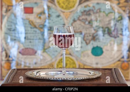 wine glass on silver platter on wooden table with ancient world map as background Stock Photo