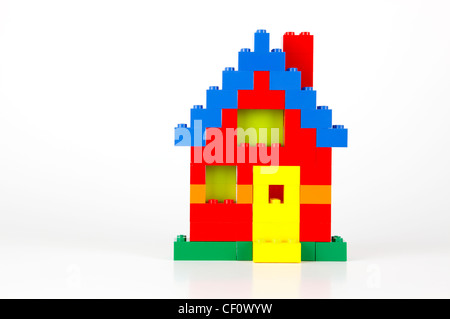 A house built of red, blue, yellow, and green traditional LEGO bricks on a white background with slight reflections and shadows Stock Photo