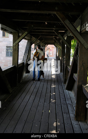 A couple of tourists on the wooden footbridge bridge called 'Executioner's Walk' across the river Pegnitz in Nuremberg, Germany. The long red-tiled Stock Photo