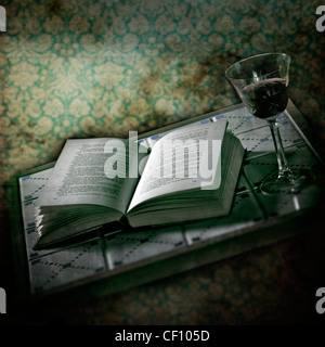 an open book on a table with old tiles and a glass of red wine in a room with an old wallpaper Stock Photo