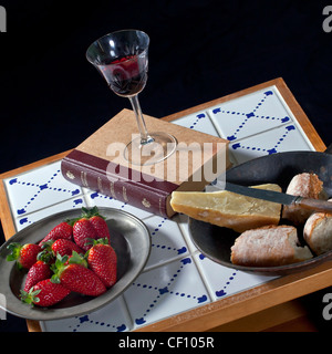 cozy snack: a book on a table made of old tiles with red wine, strawberries, cheese and bread Stock Photo