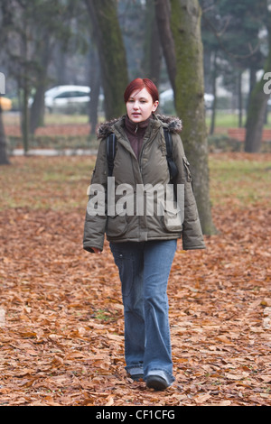 Redheaded backpacker girl walking in an autumn park. Stock Photo