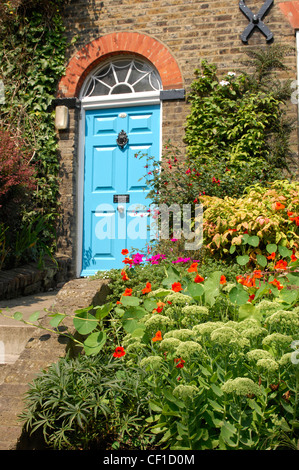 Blue painted front dowith black knocker, letterbox and knob, semi circle arch window above dowith red brick arch and ivy Stock Photo