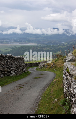 Single track road winding downhill between traditional stone walls in the Snowdonia National Park. Stock Photo