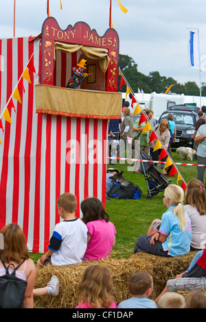 Children sitting on bales of straw enjoying a Punch and Judy show at Frampton Country Fair. Stock Photo