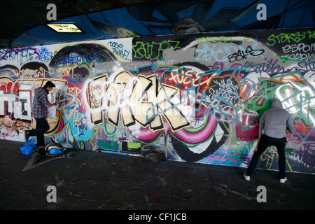 Graffiti artists at work in an area known as the under-croft on the South Bank in London. Stock Photo