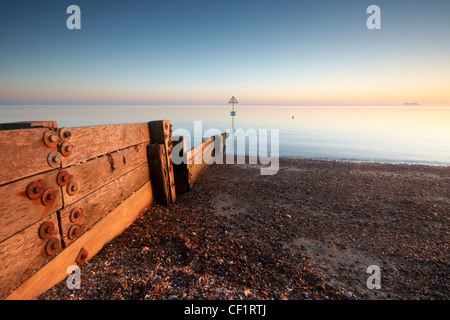 A groyne leading from the beach into tranquil waters at West Mersea in the Thames Estuary at sunset. Stock Photo