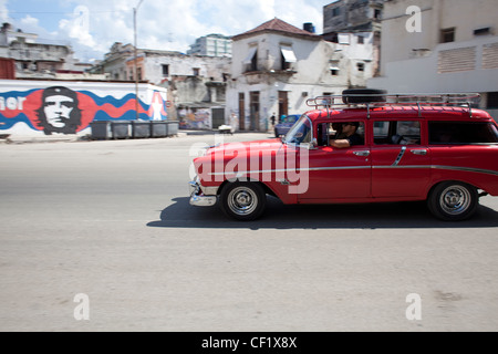 Red classic car being driven on the street in Havana, Cuba with image of Che Guevara in the background Stock Photo