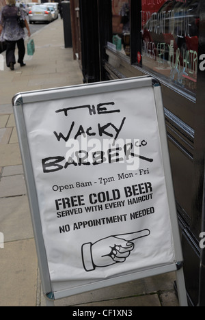 A sign on a pavement advertising the Wacky Barber company offering a free cold beer with every haircut. Stock Photo