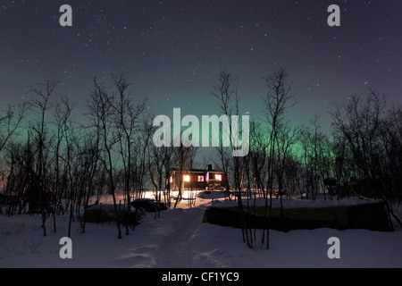 Northern lights or Aurora Borealis create a spooky Halloween green glow over a house in Abisko, Sweden within the arctic circle Stock Photo