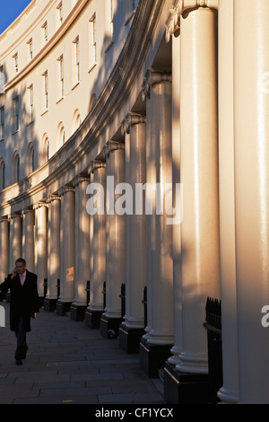 A man wearing a suit walking past stuccoed terraced houses on Park Crescent whilst talking on his mobile phone. Stock Photo
