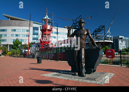 Bronze statue of a coal miner by the lightship Helwick LV14 in Cardiff Bay. The lightship was restored in 1993 and now acts as a Stock Photo