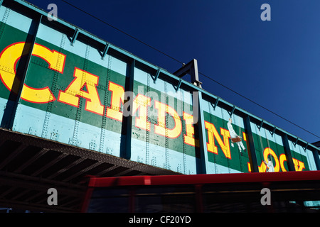 A red double decker bus passing under the old railway bridge over Chalk Farm Road at Camden Lock. The bridge features a 'trompe Stock Photo
