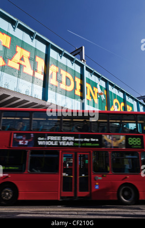 A red double decker bus passing under the old railway bridge over Chalk Farm Road at Camden Lock. The bridge features a 'trompe Stock Photo