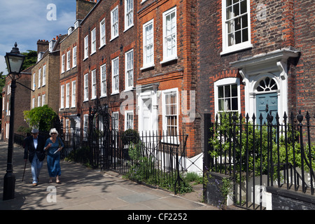 An elderly couple walking past elegant terraced houses in Church Row, Hampstead, one of the most complete Georgian streets in Lo Stock Photo