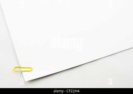 Closeup of a yellow plastic paper clip on empty paper sheets Stock Photo