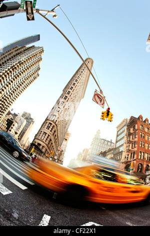 The Flatiron wedge shaped building in New York shooting into the sun long shadows traffic lights bright sunny day busy rush hour Stock Photo