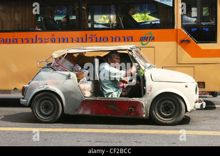 A fully loaded old car and a modern BMTA (Bangkok Metropolitan Transit Authority) bus share a street in Bangkok, Thailand. Stock Photo