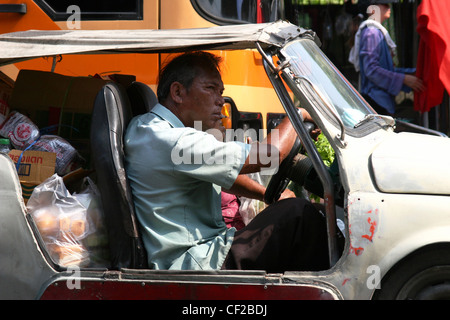 A man is driving a fully loaded old jalopy (car) on a city street in Bangkok, Thailand. Stock Photo