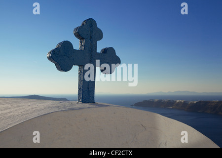A blue cross perched on top of a church with the village of Oia beyond Stock Photo