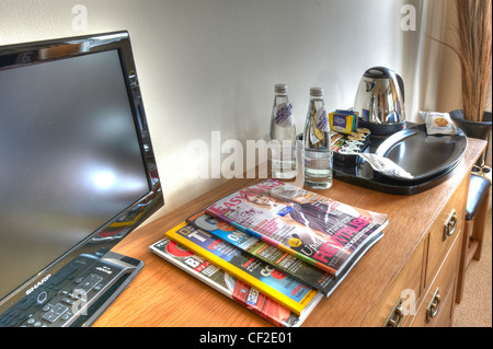 A hotel room interior showing close up of the items on top of a chest of drawers, including, magazines, television, coffee tray. Stock Photo