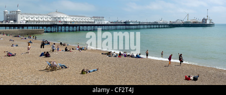 People relaxing on the pebble beach by Brighton Pier. Stock Photo