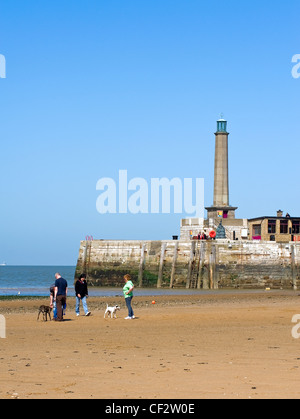 Dog walkers on the sandy beach at low tide with Margate lighthouse in the background. Stock Photo