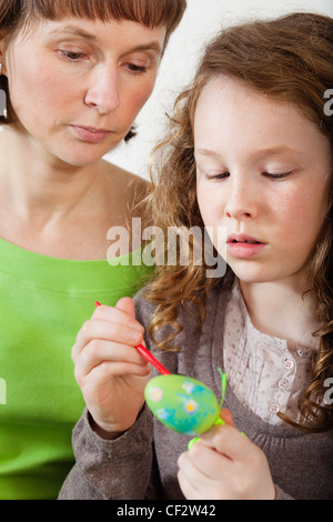 Mother and daughter sitting at home together and painting easter eggs Stock Photo