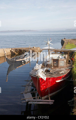 A fishing boat and replica Viking boat in Corrie Harbour on the Isle of Arran. Stock Photo