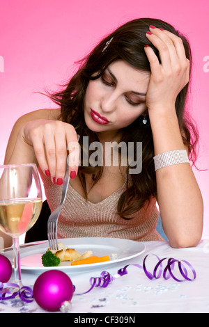 Female long brunette hair diamante hairclip wearing gold halterneck top sitting at table in front of plate small pieces of Stock Photo