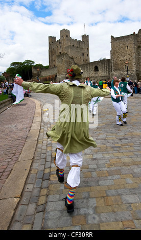 A Morris dancing fool and female morris dancers performing outside Rochester castle at the annual Sweeps Festival in Medway. Stock Photo