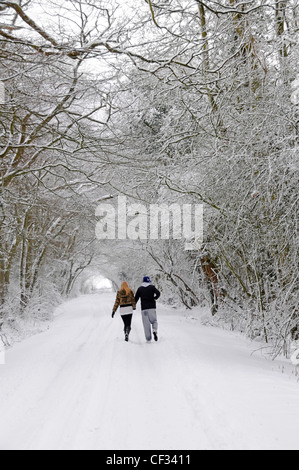 Young couple walking hand in hand along country lane after heavy snowfall Stock Photo