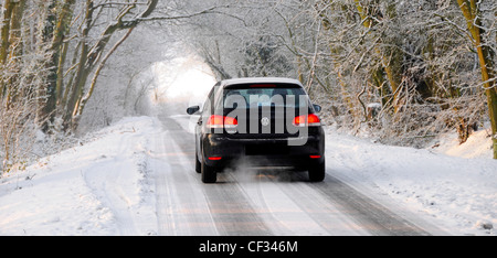 Winter landscape & Volkswagen car driving slowly through white woodland countryside along icy snow covered narrow road Brentwood Essex England UK Stock Photo