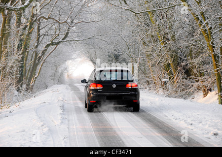 Winter weather wonderland VW Volkswagen Golf car driving on snow & ice covered road through archway of white trees Essex England UK Stock Photo