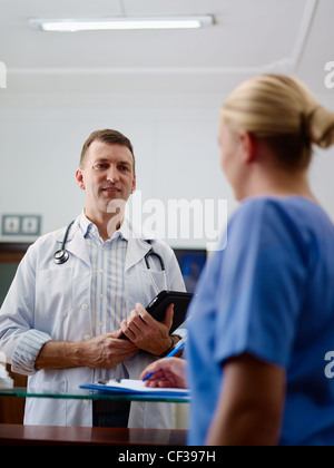 Doctor talking to young woman at work as nurse in medical clinic and taking medical file. Stock Photo