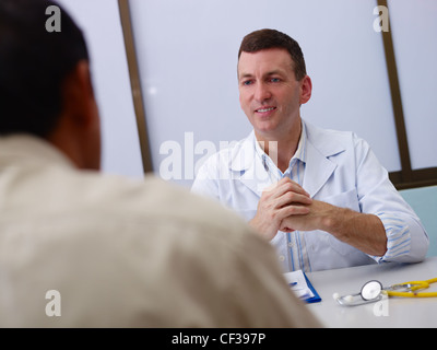 Friendly doctor working and giving assistance to old male patient in hospital office. Focus on background Stock Photo