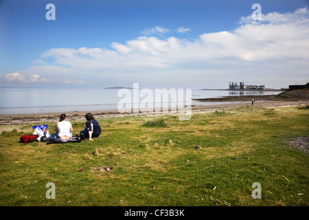 Two people sitting on the grass looking out to sea at Granton Harbour in Edinburgh. Stock Photo