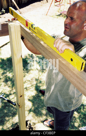 FORBuild a Tree House Step Male aligning a plank of wood using a spirit level Stock Photo