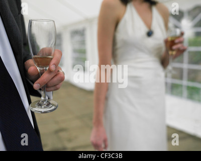 Close up of a man holding a nearly empty glass with a woman in white holding a full glass of champagne. Stock Photo