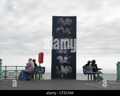 A sculpture of people kissing with two couples sitting either side on the water front in Brighton. Stock Photo