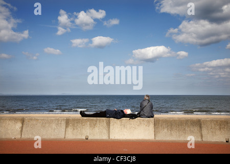 A senior couple relaxing on the promenade of Portobello beach along the coast of the Firth of Forth. Stock Photo