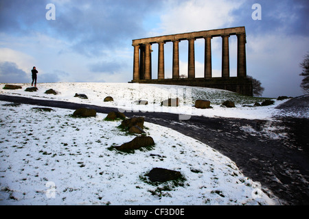 A woman walking in the snow by the Scottish National Monument on Calton Hill. Stock Photo